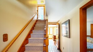 A staircase with carpeted steps leading to a door, a tiled floor, and a framed picture on the wall. - New Seabury Getaway | Perfect Leaf Peeping! (Mashpee)