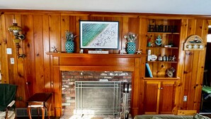 A cozy living room with a fireplace, wooden paneling, a television, and a bookshelf. - New Seabury Getaway | Perfect Leaf Peeping! (Mashpee)
