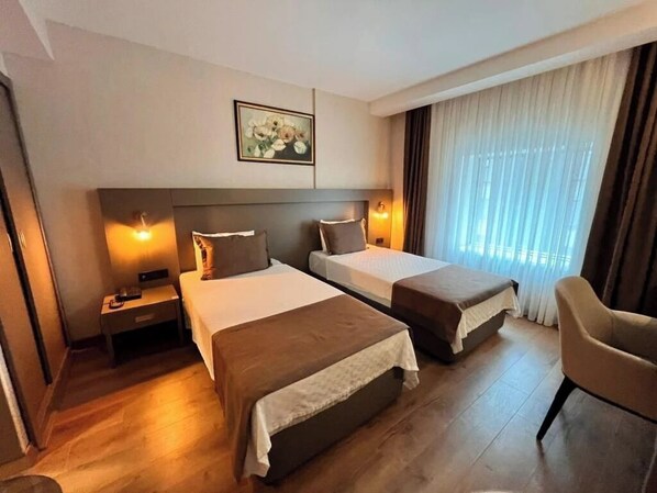 Habitación de hotel con dos camas, una mesita de noche, una silla y un cuadro en la pared.
