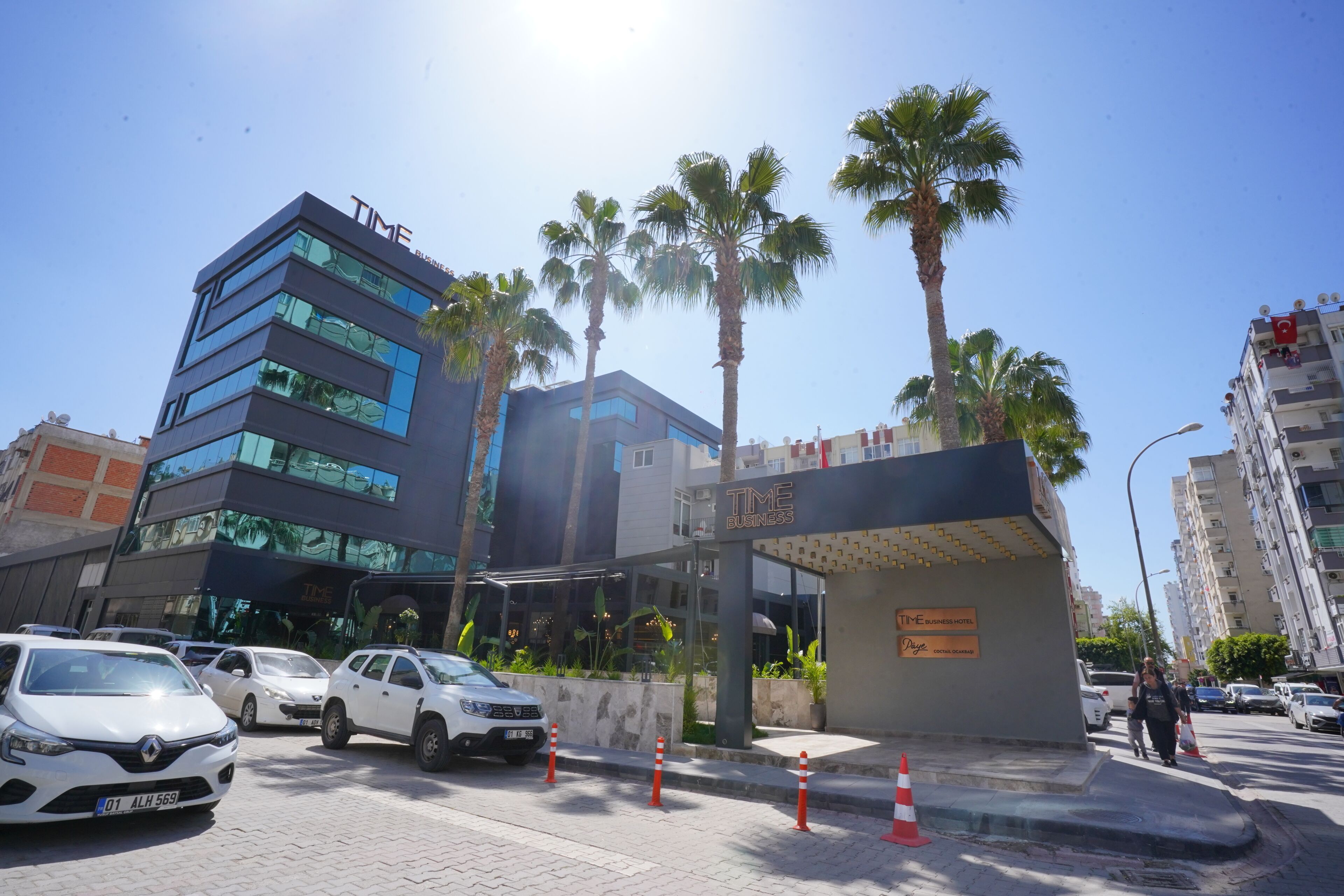 A modern building with a glass facade, palm trees, and a sign for 'TIME Business Hotel.'