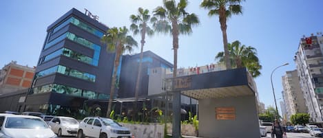 Un edificio moderno con fachada de vidrio, palmeras y un letrero que dice 'TIME Business Hotel'.