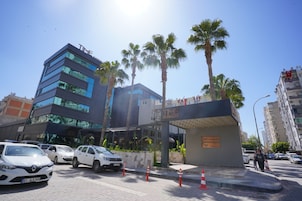 Un edificio moderno con fachada de vidrio, palmeras y un letrero que dice 'TIME Business Hotel'.
