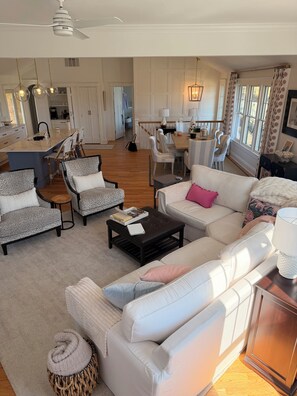 A spacious living room with a large sofa, armchairs, a coffee table, and a dining area with a chandelier.