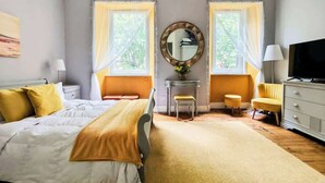 Quarto com cama, mesas de cabeceira, penteadeira, espelho e televisão.