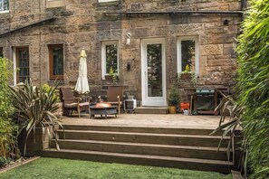 Ein Steinhaus mit einer Terrasse, die Gartenmöbel, einen Grill und Kübelpflanzen bietet.