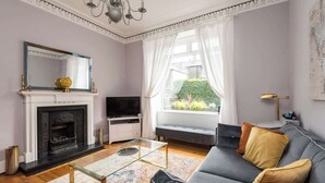Sala de estar com lareira, sofá, TV e vista para o verde lá fora.
