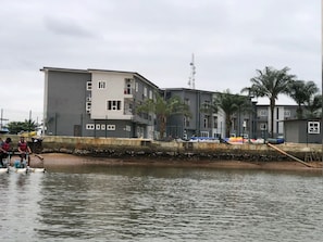 A multi-story building with balconies, a water body in the foreground, and palm trees. - Pearl Paradise Resort by 4E (Bonny)