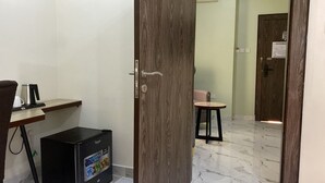 A room with a wooden door, a small table with a chair, a black refrigerator, and a white wall. - Pearl Paradise Resort by 4E (Bonny)
