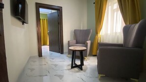 A living room with a marble floor, two armchairs, a small round table, and a television on the wall. - Pearl Paradise Resort by 4E (Bonny)