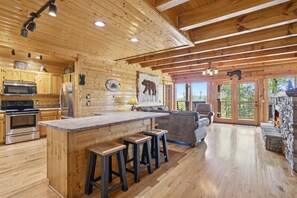 Ein Holzblockhaus-Innenraum mit Küche, Bar, Kamin aus Stein und großen Fenstern.