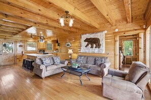 Ein Interieur einer Holzhütte mit Essbereich, zwei Sofas, einem Couchtisch und einer Bärenmalerei an der Wand.