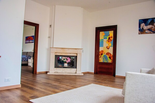 A living room with hardwood flooring, a fireplace with a vase of flowers, and two doors with colorful artwork.