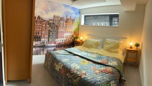 Une chambre à coucher comprenant un lit, une table de chevet, une lampe fixée au mur et une fenêtre avec des stores.