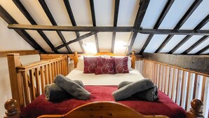 Ein Bett mit Holzboden, eine rote Decke und Kissen, ein hölzernes Kopfteil und eine schräge Decke mit sichtbaren Balken.