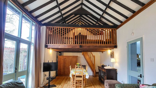 Ein großzügiges Loft mit freiliegenden Holzbalken, einem Essbereich mit Tisch und Stühlen sowie einer gemütlichen Sitzecke mit Sofas und einem gemusterten Teppich.