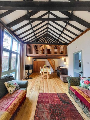 Ein großzügiges Loft mit freiliegenden Holzbalken, einem Essbereich mit Tisch und Stühlen sowie einer gemütlichen Sitzecke mit Sofas und einem gemusterten Teppich.
