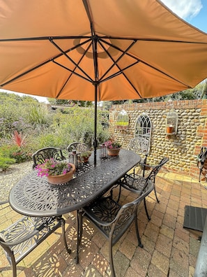 A patio with a round metal table, four chairs, and a large brown umbrella. - Nicholson Cottage  - sleeps 4 guests  in 2 bedrooms (Happisburgh)
