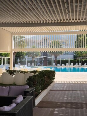 Ett takförsett utomhusområde med en pool, solstolar och en sittgrupp.