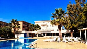 A swimming pool with clear blue water, surrounded by lounge chairs and palm trees. - FRUIT VILLAGE DIAMANTE Dominicus (Grisolia)