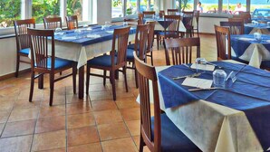 A restaurant with multiple tables and chairs, large windows with a view of the sea, and a tiled floor. - FRUIT VILLAGE DIAMANTE Dominicus (Grisolia)