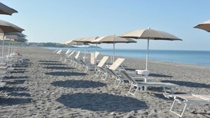 A beach with rows of white lounge chairs and beige umbrellas. - FRUIT VILLAGE DIAMANTE Dominicus (Grisolia)
