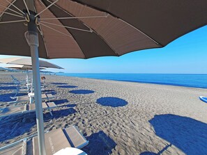 A beach with sun loungers and umbrellas, a clear sky, and the ocean in the background. - FRUIT VILLAGE DIAMANTE Dominicus (Grisolia)