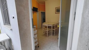 Una stanza con un tavolo da pranzo e sedie, un piccolo finestrino e una porta che dà su un'altra stanza.