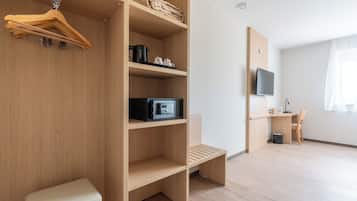 Een moderne, goed verlichte kamer met een houten garderobe, een bankje, een bureau met stoel, en een televisie.