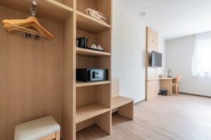 A modern, well-lit room with a wooden wardrobe, a bench, a desk with a chair, and a television. - The Originals City, Hôtel du PAarc, Gravelines (Gravelines)