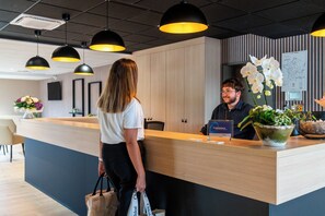 A reception desk with a wooden counter, black pendant lighting, and a wall-mounted map. - The Originals City, Hôtel du PAarc, Gravelines (Gravelines)