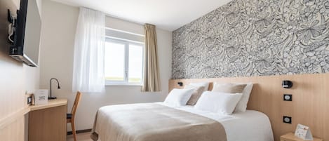 Habitación de hotel con cama, escritorio, silla, televisor y ventana con cortinas.