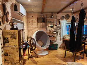 Une pièce chaleureuse aux murs en bois, avec un grand fauteuil rond, un rouet et divers objets suspendus.
