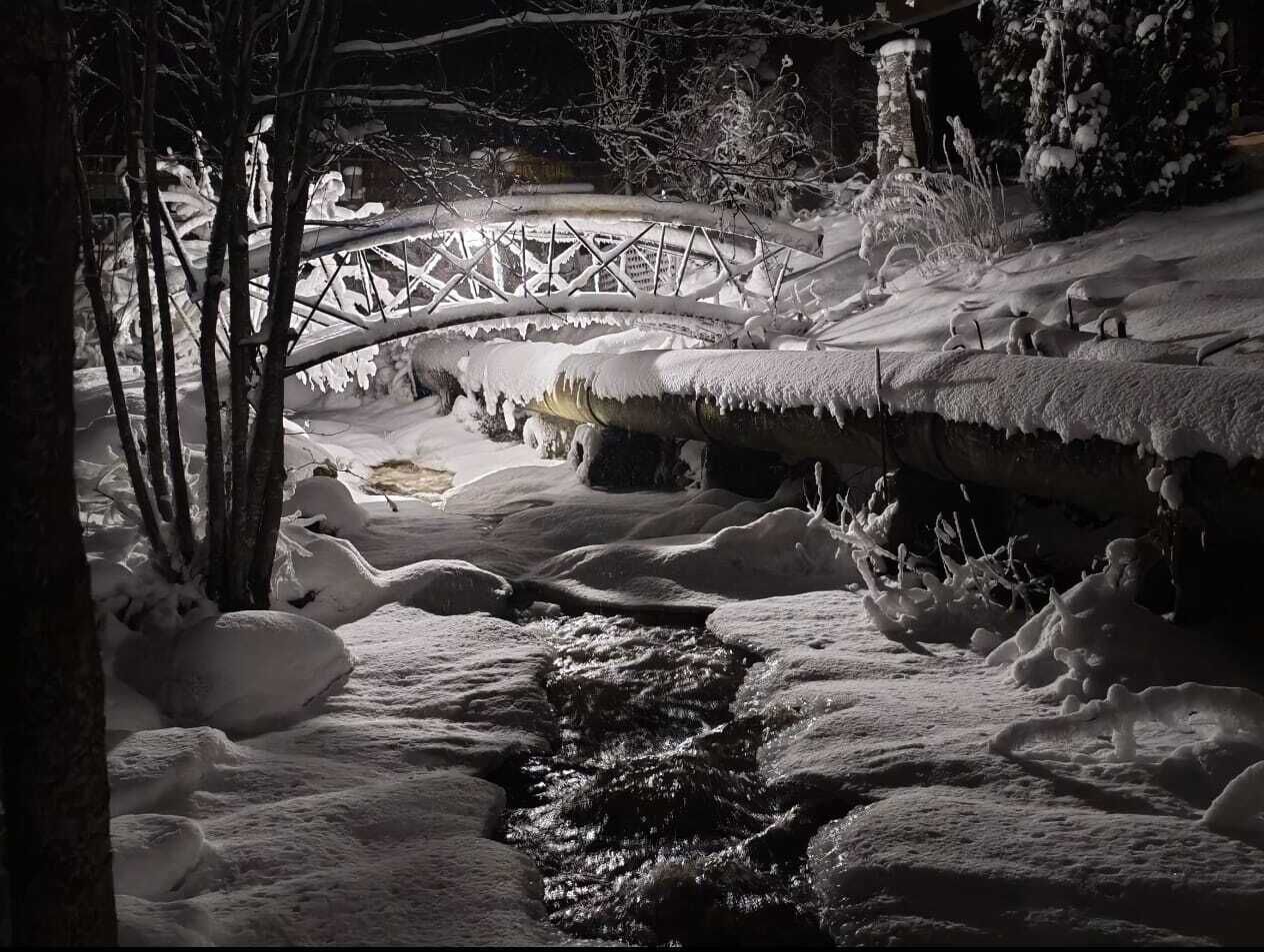 A snow-covered landscape with a bridge and a stream.