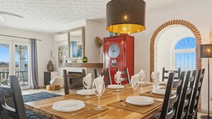 A dining area with a wooden table set for six, a red cabinet, and a large window with an arched view. - Amazing villa los pajaritos with stunning views - Ref 50 (Las Lagunas de Mijas)