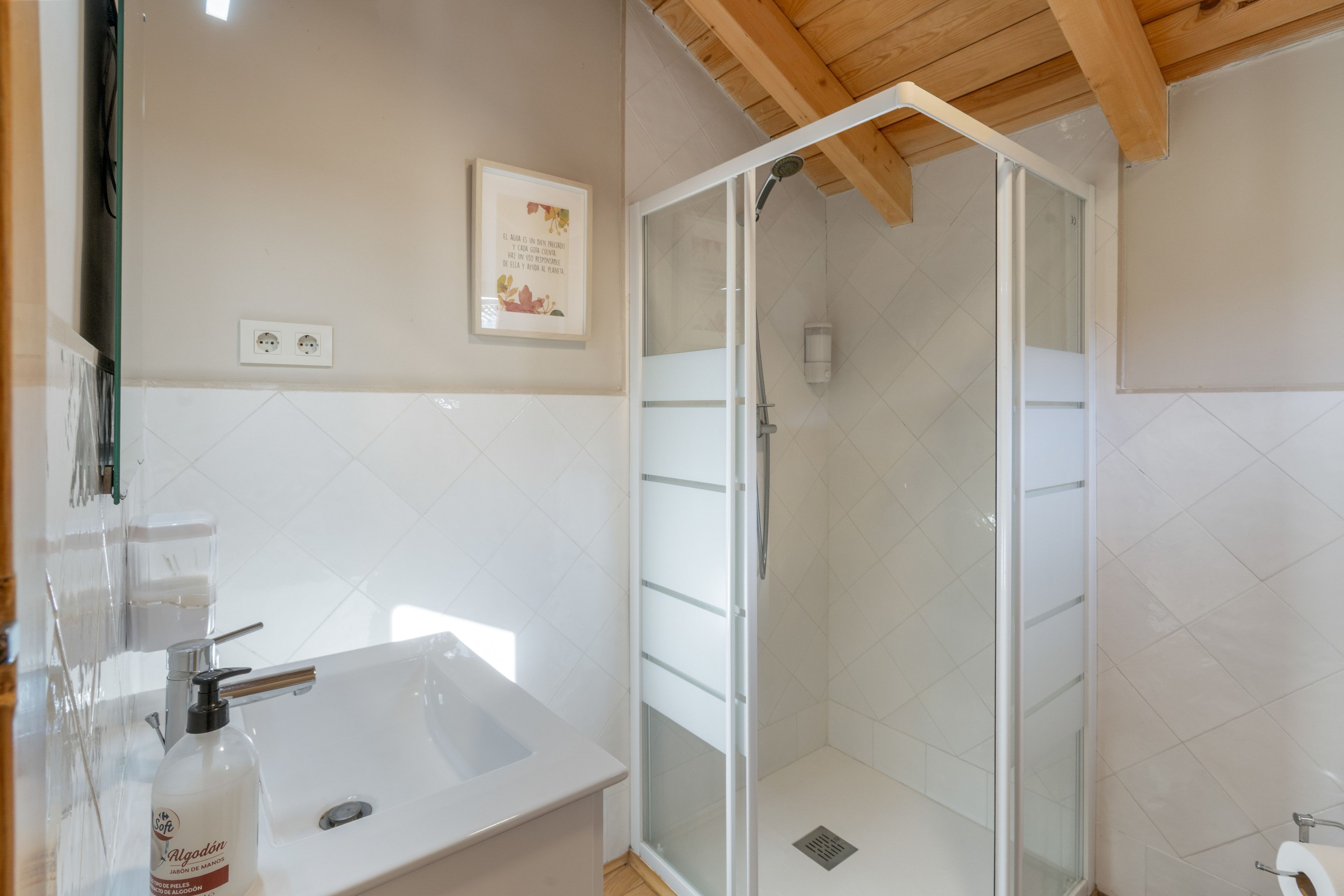 Un baño con ducha, lavabo y una cita enmarcada en la pared.