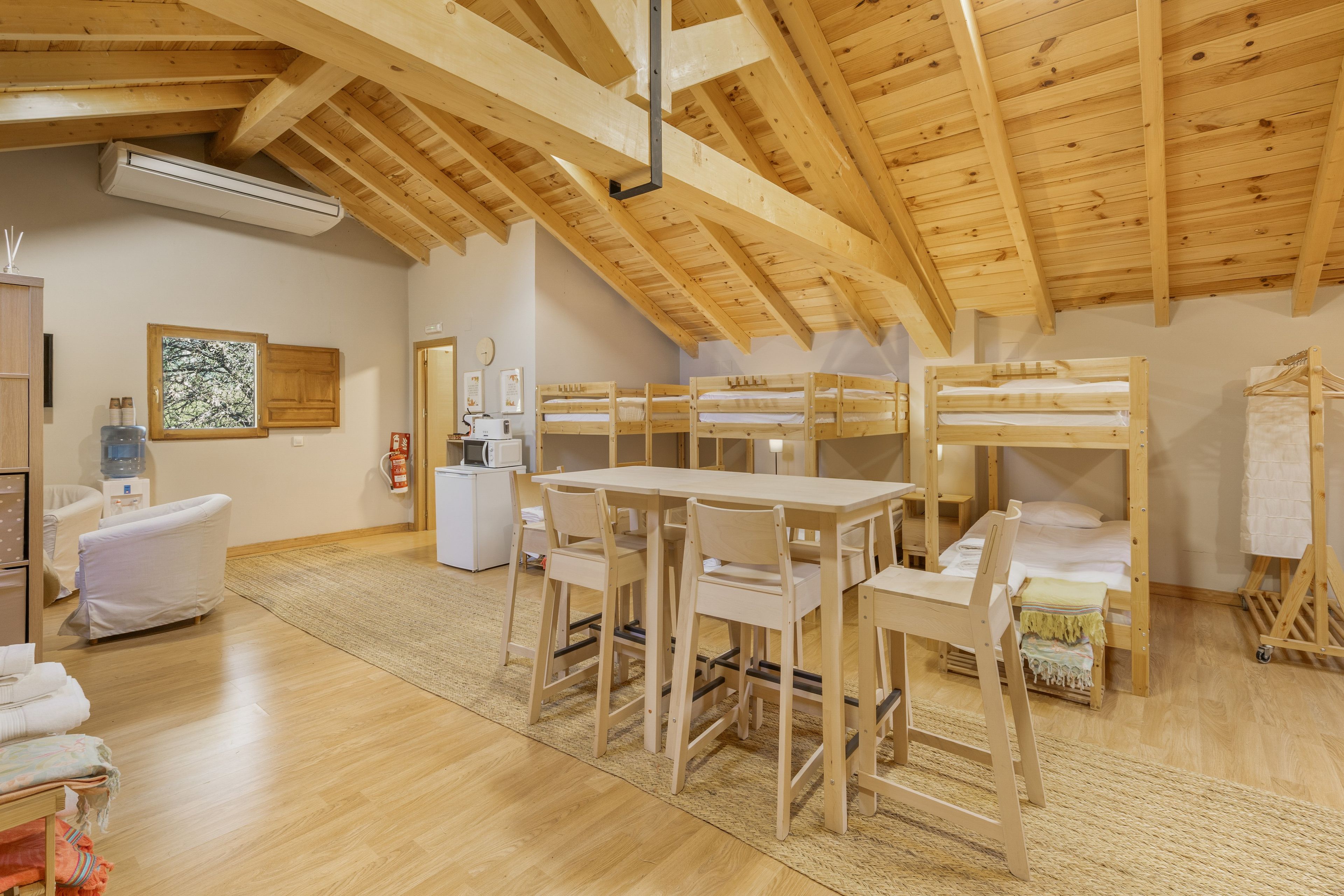 A room with bunk beds, a dining table, chairs, a water dispenser, and a small kitchenette.