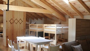 A spacious loft with a high ceiling, exposed wooden beams, a central dining table with chairs, a sofa, and a bunk bed. - The Rural Hostel in Mombeltrán, Ávila, Tiétar Valley (Mombeltrán)