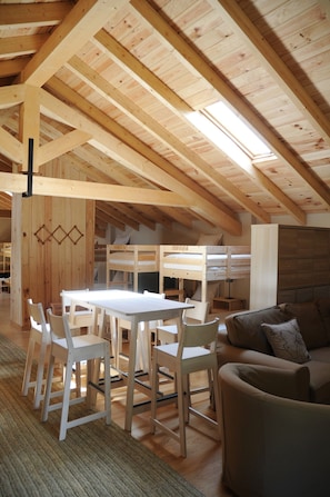 A spacious loft with a high ceiling, exposed wooden beams, a central dining table with chairs, a sofa, and a bunk bed. - The Rural Hostel in Mombeltrán, Ávila, Tiétar Valley (Mombeltrán)