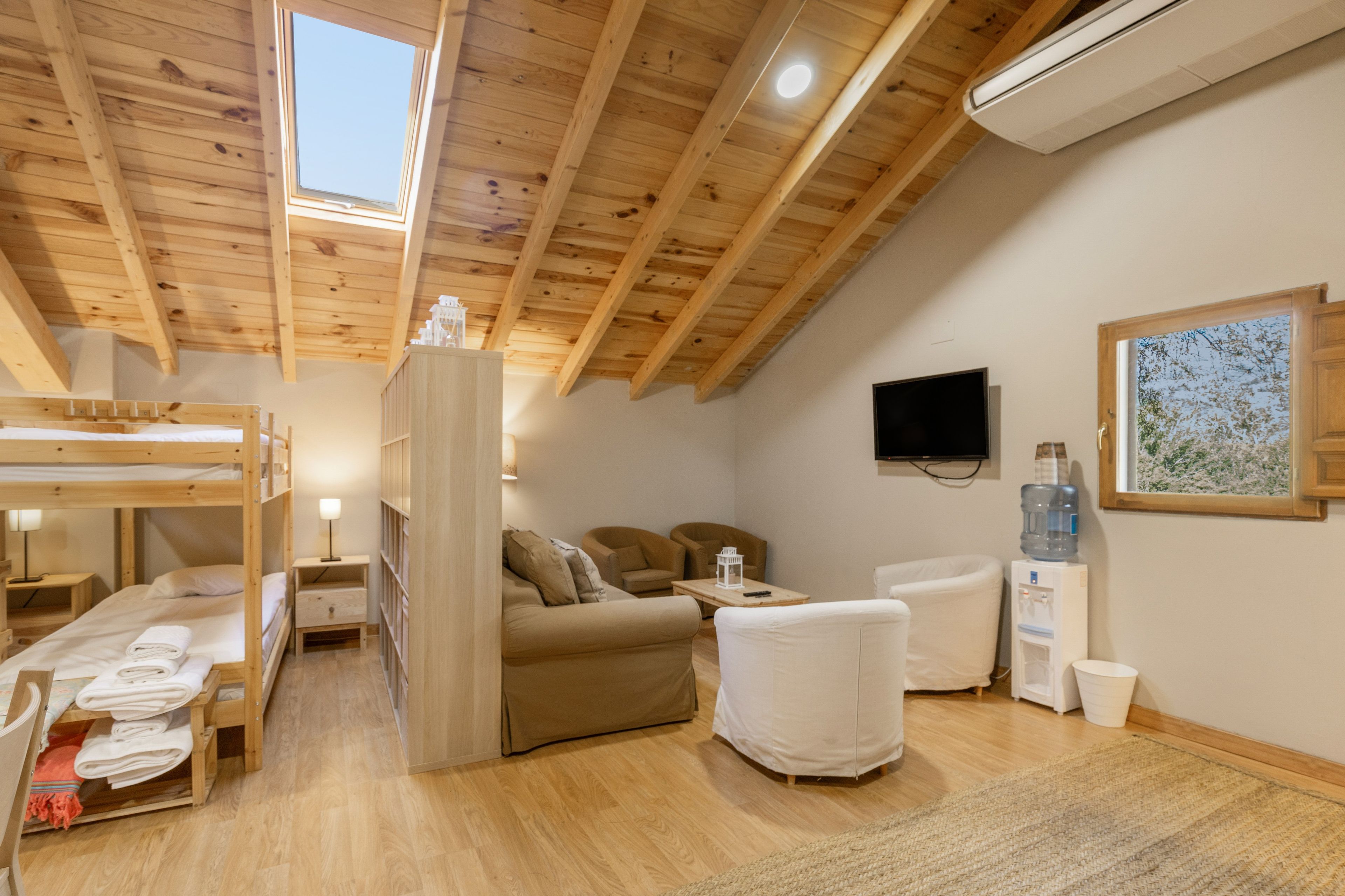 Una habitación acogedora con una cama litera, un sofá, un televisor y un dispensador de agua.
