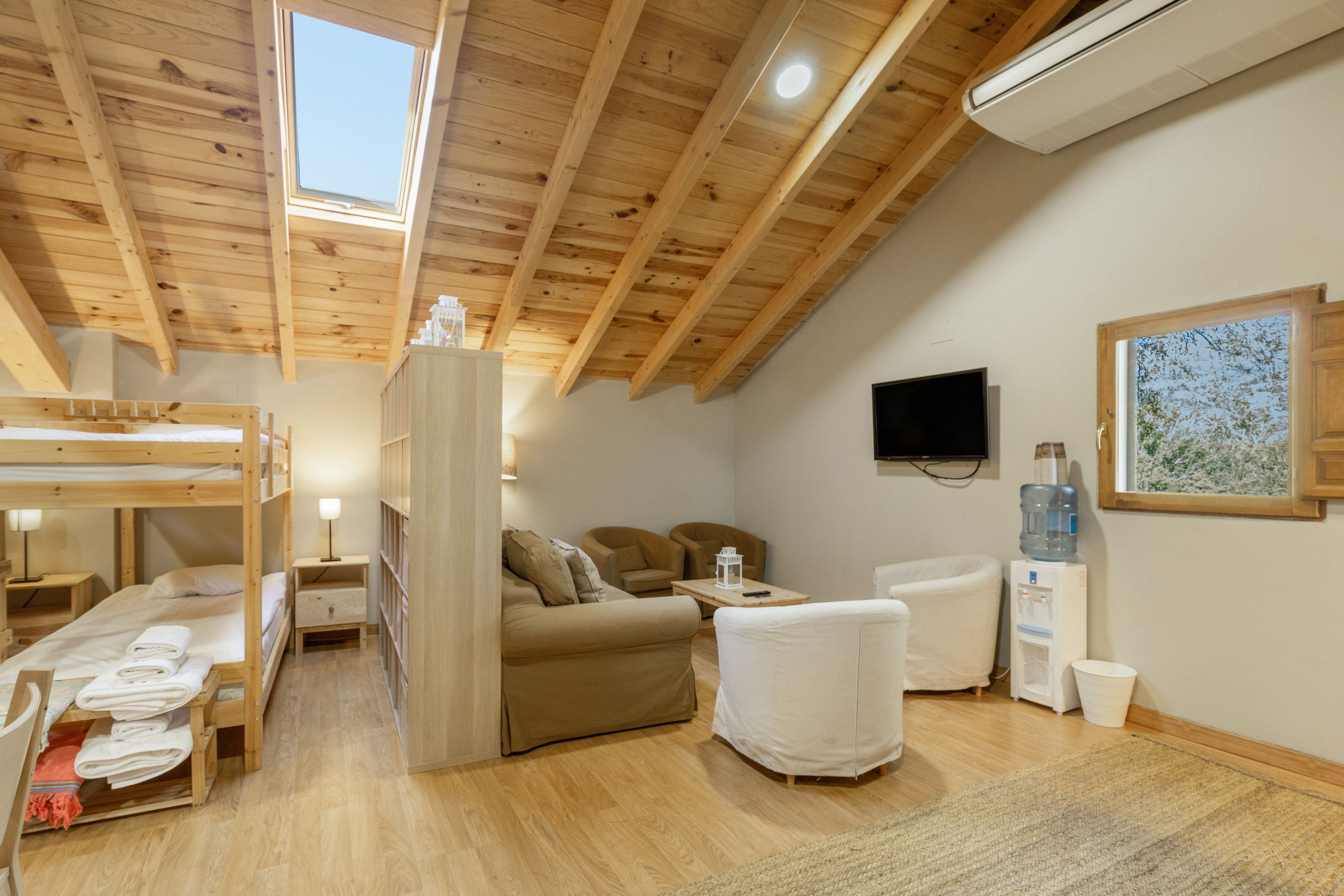 A cozy room with bunk beds, a sofa, a television, and a water dispenser.
