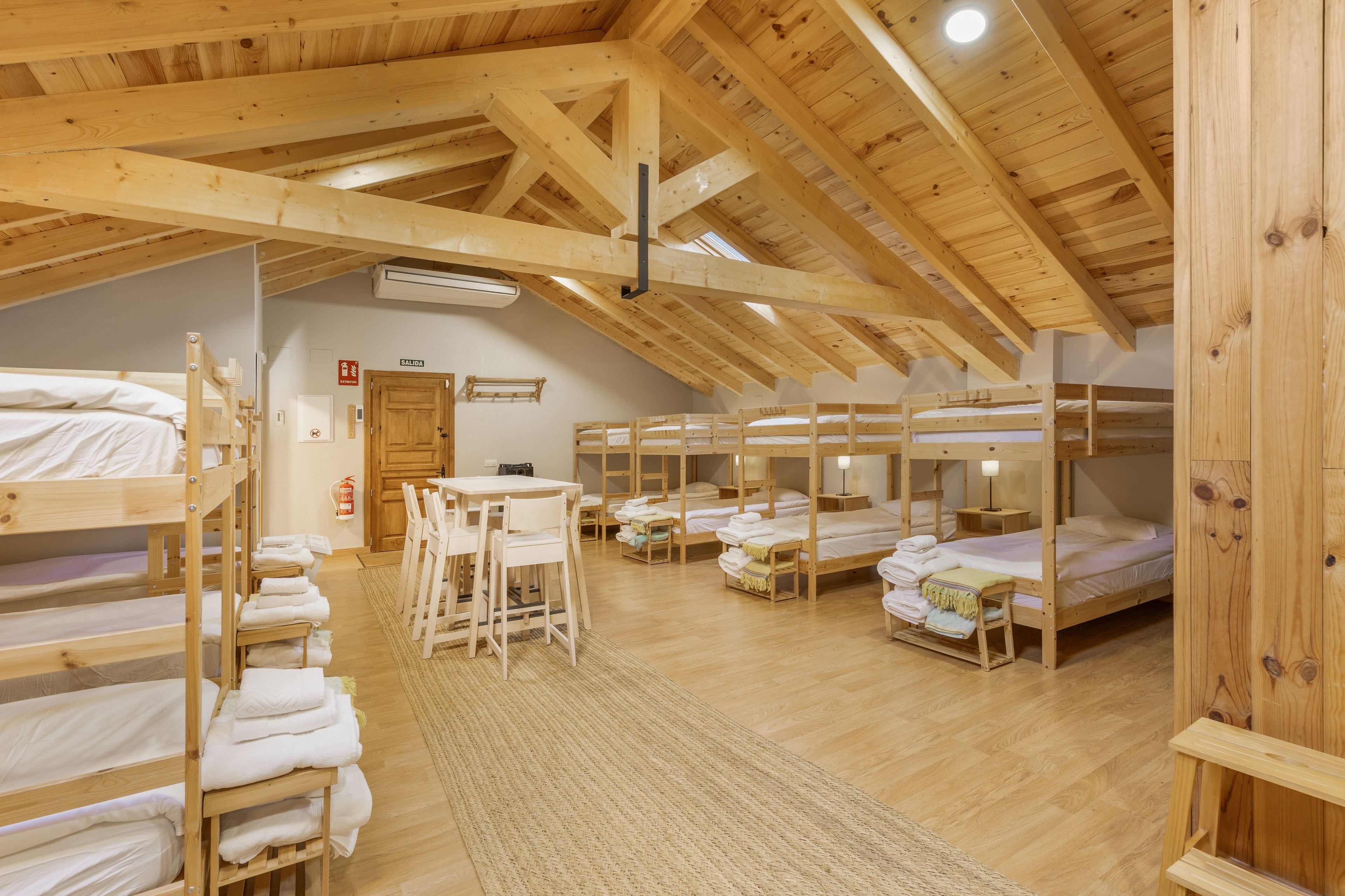 Un intérieur en bois avec des lits superposés, une table, des chaises et un panneau indiquant la sortie.