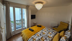 A hotel room with a bed, a chair, a TV, and a balcony. - Royal Crown Apartment With Royal Garden (Le Bourget)