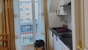 A compact kitchen with a washing machine, a sink, and a window with curtains. - Royal Crown Apartment With Royal Garden (Le Bourget)
