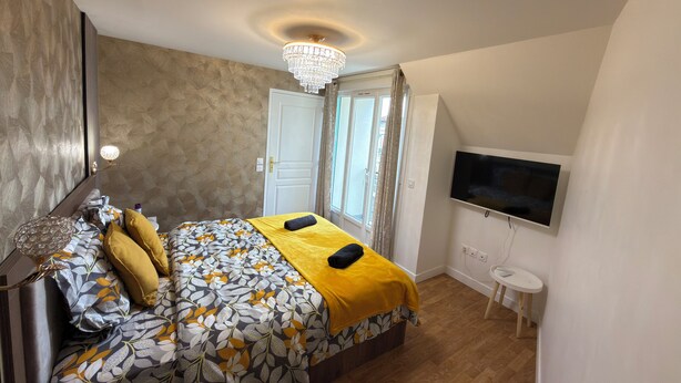 A bedroom with a bed, a TV, a small table, and a chandelier. - Royal Crown Apartment With Royal Garden (Le Bourget)