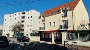 A residential street with a two-story building featuring a red-tiled roof and a balcony. - Royal Crown Apartment With Royal Garden (Le Bourget)