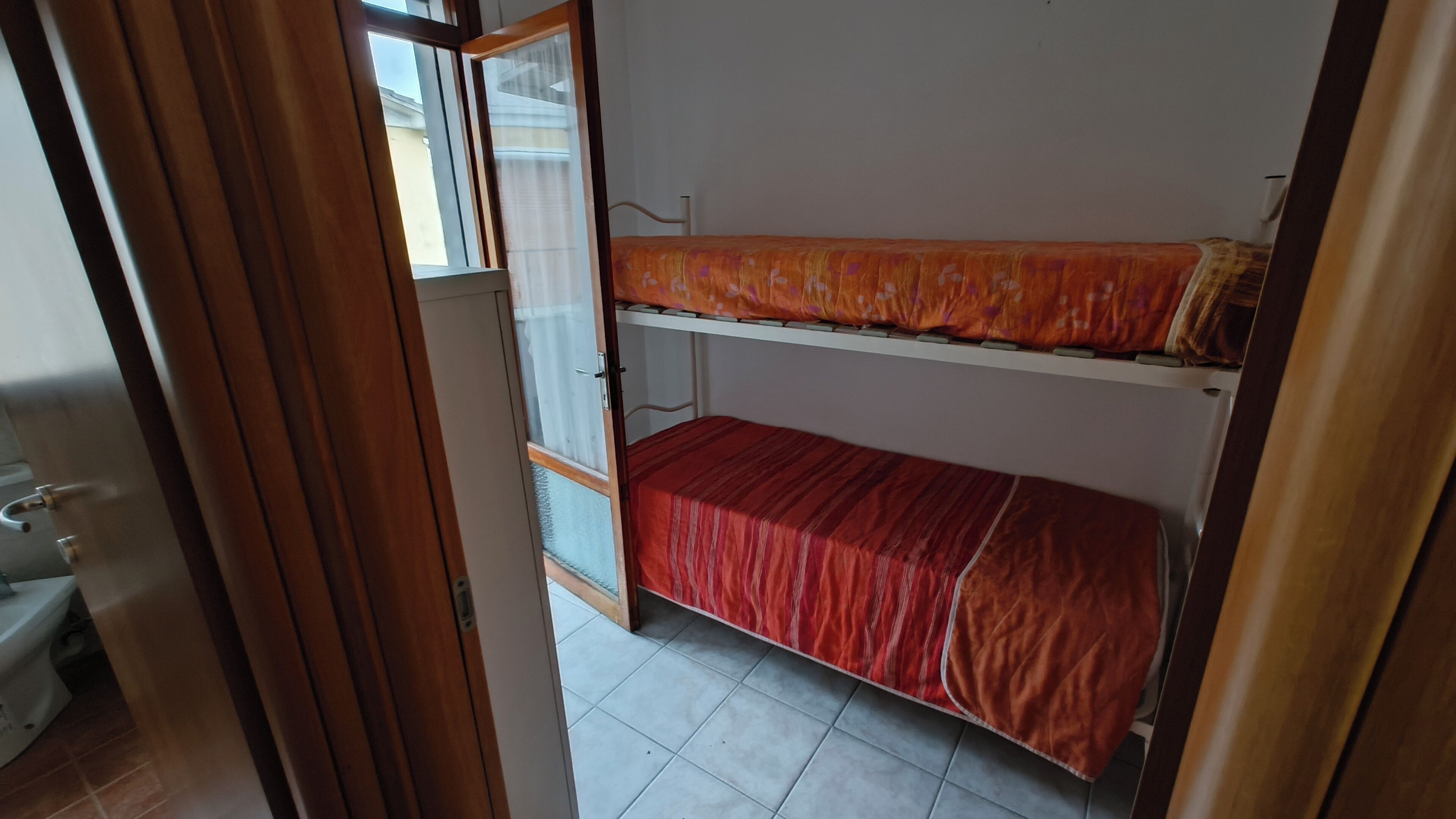 A room with a bunk bed, a window with curtains, and a door leading to a bathroom.