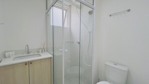 Un baño moderno con ducha envuelta en vidrio, inodoro y lavabo con espejo.
