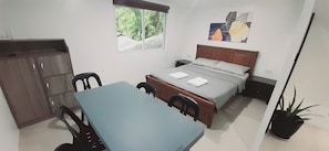 Une petite pièce bien éclairée, avec un lit simple, un bureau et une chaise. Une fenêtre offre une vue sur la verdure environnante.