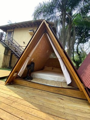 A triangular wooden tent with a mattress inside, set on a wooden deck. - Cabanas Mountain (São Sebastião)