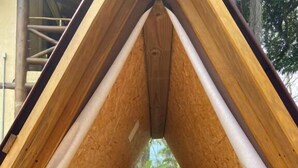 A small, triangular wooden tent with a bed, a fan, and a view of trees through a window. - Cabanas Mountain (São Sebastião)